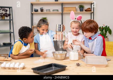 Kinder, die Schürze tragen, surfen auf einem digitalen Tablet im Internet, um ein Rezept für appetitliche Kekse zu finden Stockfoto