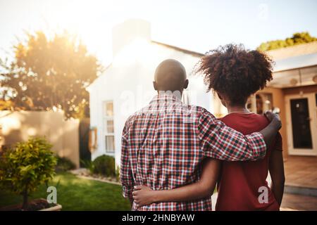 Was für ein schöner Ort, um unser Zuhause zu nennen. Rückansicht eines jungen Paares, das sein neues Haus draußen bewundert. Stockfoto