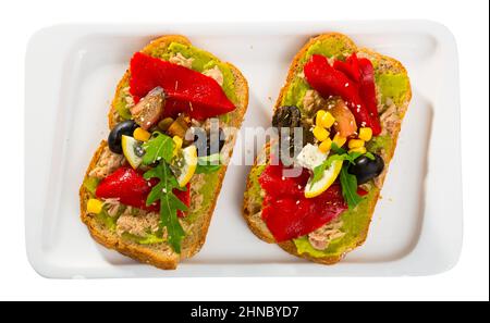 Draufsicht auf Sandwiches mit Guacamole, Thunfisch in der Dose, Gemüse auf weißem Teller Stockfoto