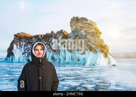 Teenager-Tourist in einer Kapuze sitzt auf dem gefrorenen Eis des Baikalsees. Stockfoto