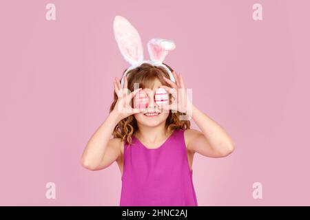 Entzücktes Kind, das während der Osterparty im pinken Studio das Auge mit Eiern bedeckte Stockfoto