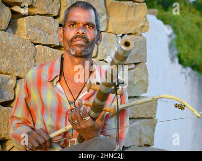 Der indische Straßenmusiker spielt bei Sonnenuntergang seine traditionelle Ravanahatha (altes indisches Saiteninstrument) und schaut auf den Zuschauer. Stockfoto