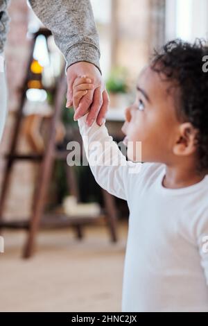 Nahaufnahme eines schwarzen Jungen, der die Hand der Mutter hält, während er zu Hause mit ihr geht Stockfoto