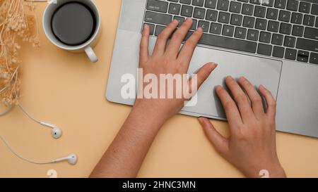 Overhead-Aufnahme, Focus Hands, Eine Frau, die am Laptop-Computer arbeitet und auf der Notebook-Tastatur auf beigem Hintergrund tippt. Stockfoto