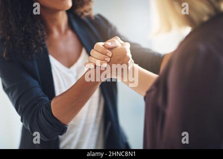 Hand in Hand auf dem Weg zum Erfolg. Eine kurze Aufnahme von zwei Geschäftsfrauen, die sich bei der Arbeit solidarisch die Hände schüttelten. Stockfoto