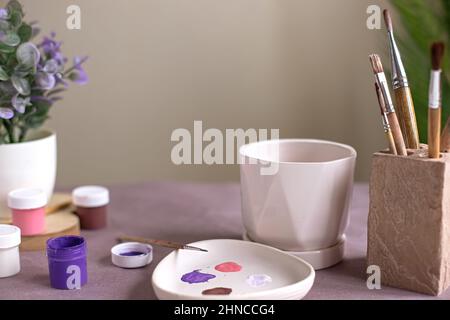 Ein Stillleben mit einem weißen Keramik-Blumentopf steht auf einem Tisch mit Bastelwerkzeugen Stockfoto