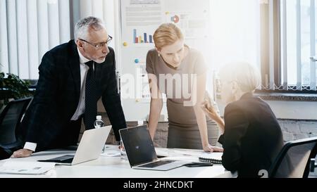 Reife Geschäftsfrau, die während der Besprechung im Büro mit dem Finger in die Nähe von Kollegen zeigt Stockfoto