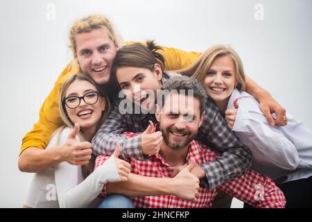 Glückliche Firmenstudenten beste Freunde machen Selfies. Gruppe junger Menschen posiert zusammen mit Daumen nach oben. Multiethnisches Geschäftsteam. Lächelnde Gruppe von Stockfoto