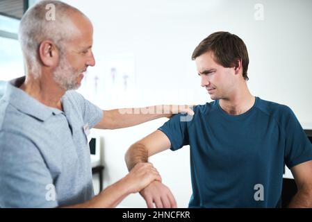 Genau dort ist der Schmerz. Kurzer Schuss eines hübschen reifen männlichen Physiotherapeuten, der einen Patienten behandelt. Stockfoto