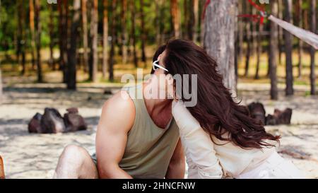 Brünette Frau in Sonnenbrille küssen Freund am Strand Stockfoto