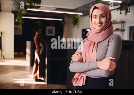 Porträt einer selbstbewussten jungen Frau aus dem Nahen Osten, die lächelt und die Kamera im Coworking Space anschaut Stockfoto