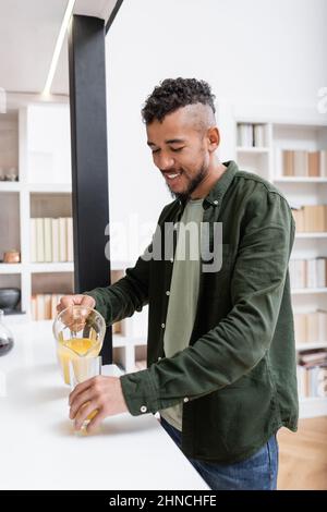 Ein zufriedener afroamerikanischer Mann goss Orangensaft in Glas Stockfoto