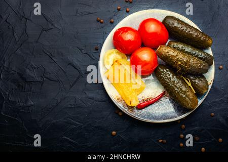 Eingelegtes Gemüse auf einem Teller. Eingelegte Gurken, Tomaten und Paprika. Speicherplatz kopieren Stockfoto