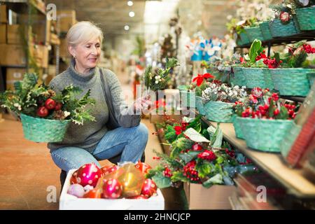 Lächelnde ältere Frau, die Weihnachtsdekorationen im Geschäft auswählt Stockfoto