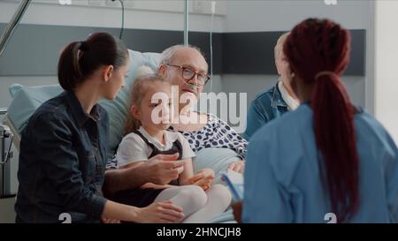 Nahaufnahme einer afroamerikanischen Krankenschwester, die mit dem Patienten und seiner Familie auf der Krankenstation spricht und Diagnose und Behandlung erklärt. Assistent, der mit Menschen und Verwandten über die Gesundheitsversorgung diskutiert. Stockfoto
