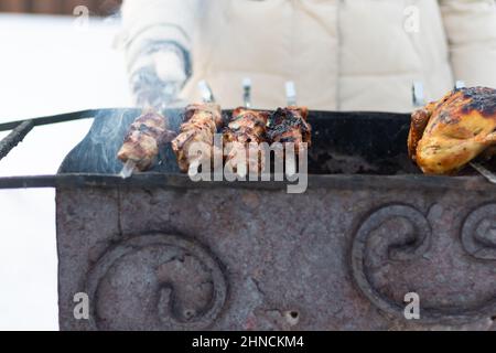 Eine Frauenhand in einem Fäustling fritiert an einem sonnigen Wintertag einen Grill auf dem Grill in der Natur. Selektiver Fokus. Nahaufnahme Stockfoto