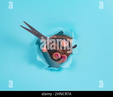 Frau Hand mit Schere in ganz zerrissenen blauen Papier Hintergrund Stockfoto