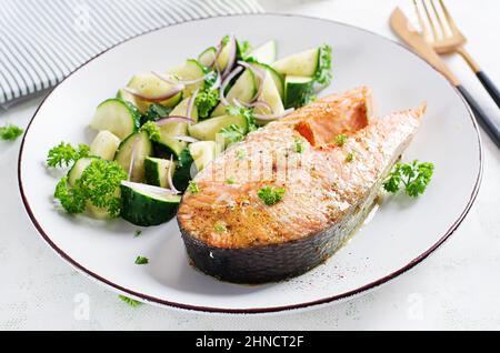 Gebackenes Lachsfischsteak und frischer Gurkensalat mit roten Zwiebeln. Stockfoto