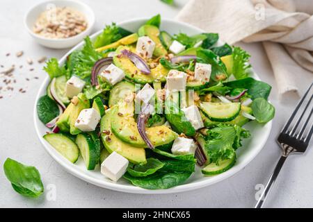 Salat mit Avocado-Nahaufnahme auf grauem Hintergrund. Vegetarischer Salat mit Gemüse, Feta und Samen. Seitenansicht. Stockfoto