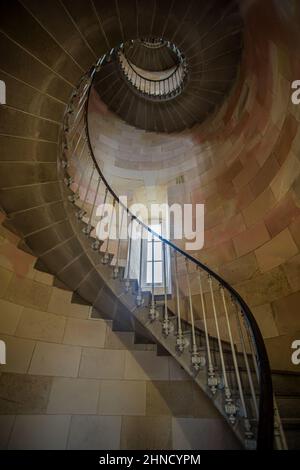 Lange Wendeltreppe mit Steintreppen und Metallgeländer in einem hohen, altmodischen Turm aus Stein mit einem kleinen Fenster in Frankreich Stockfoto