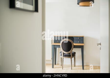 Bequemer Stuhl am klassischen schwarzen Schreibtisch an der weißen Wand im hellen Raum mit rundem Kronleuchter in der geräumigen Wohnung Stockfoto