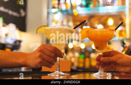 Pflanzen Sie nicht erkennbare Menschen mit Gläsern Margarita-Cocktails, garniert mit Scheiben Zitrusfrüchten, auf der Theke auf unscharfem Hintergrund Stockfoto