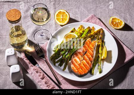 Gegrilltes Lachssteak mit gebratenem Spargel und Zitrone auf einem Teller auf einer Leinentischdecke Stockfoto