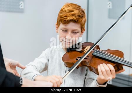 Fröhliches Ingwer-Kind spielt Geige, während es beim Musikunterricht Melodie lernt Stockfoto