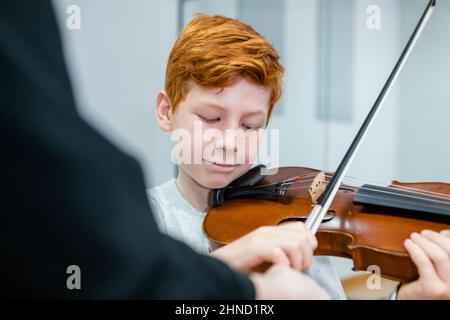 Crop-Musiklehrer in der Nähe von Rotschopf Junge mit Geige im Klassenzimmer stehen Stockfoto