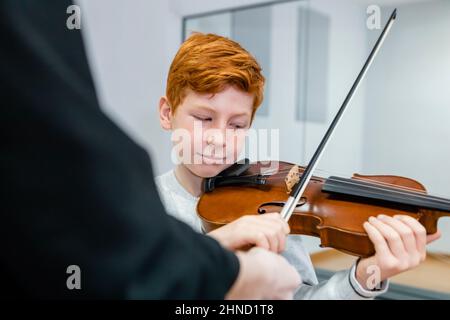 Crop-Musiklehrer in der Nähe von Rotschopf Junge mit Geige im Klassenzimmer stehen Stockfoto