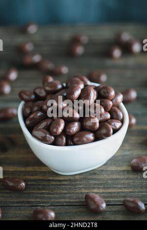 Schüssel mit schokoladenüberzogenen Rosinen oder Nüssen über einem rustikalen Holztisch. Selektiver Fokus mit verschwommenem Vorder- und Hintergrund. Stockfoto