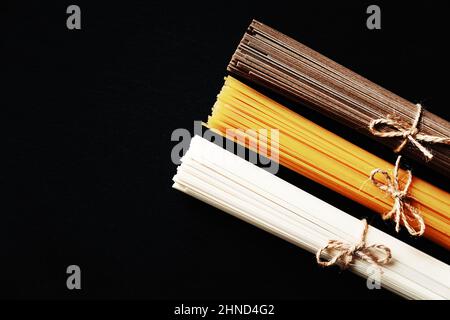 Nudeln aus verschiedenen Ländern. Soba, udon, Spaghetti. Schwarzer Hintergrund, flaches Lay, Kopierbereich. Hintergrund der Speisen. Stockfoto
