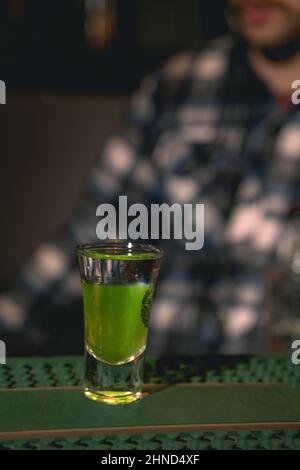 Schnapsglas mit geschichtetem Getränk Green Mexican an der Theke Stockfoto