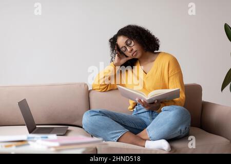 Müde junge schwarze Frau schläft mit Buch in der Nähe Laptop-Computer zu Hause, Kopierer Platz Stockfoto