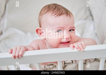 Sly Baby in einer Krippe mit einem wütenden Blick. Lustiges Kind im Bett, Alter sechs Monate Stockfoto