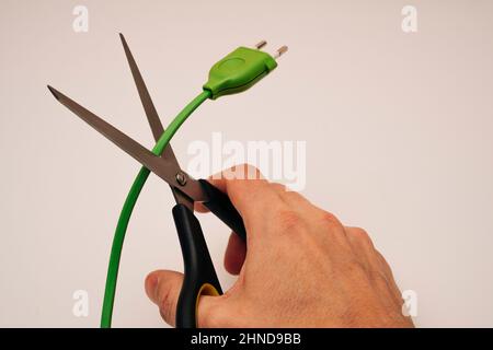 Eine Hand mit Büroschere schneidet einen elektrischen Draht, Gefahr, Verletzung, Risiko, auf einem rosa Hintergrund. Stockfoto