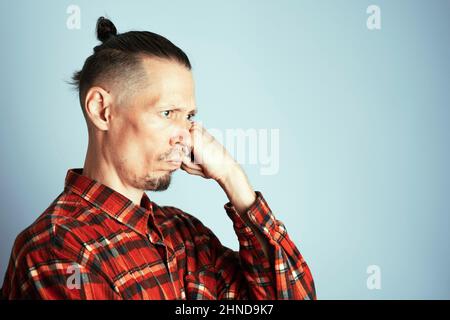 Ein Nahaufnahme-Foto eines ernsthaft nachdenklichen jungen Mannes in einem roten karierten Hemd. Ein Mann mit langen Haaren in einem Knoten gebunden, seine Wange mit der Faust. Auf einem Stockfoto