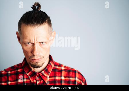 Ein Nahaufnahme-Foto eines streng rücksichtslosen, ernsthaft jungen Mannes in einem roten karierten Hemd. Ein Mann mit langen Haaren, die in einem Knoten zusammengerafft sind, oder das Brötchen eines Mannes sieht anvertrauen aus Stockfoto