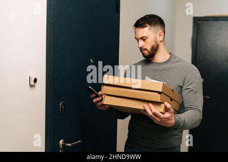 Der Lieferer stand vor der Tür der Kundenwohnung mit Schachteln mit heißer Pizza und rief den Kunden am Telefon an. Stockfoto