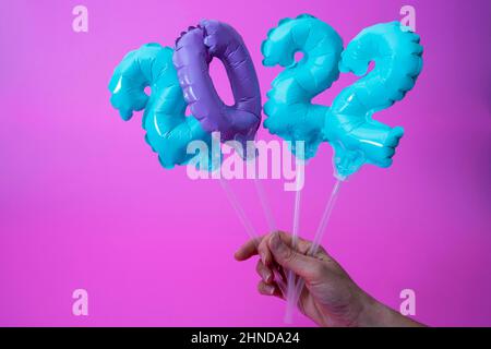 Eine Frauenhand hält aufblasbare Figuren mit den Zahlen 2022 auf purpurem Hintergrund, aufblasbare Ballons 2022, Neujahrskonzept und Weihnachtsdekor Stockfoto