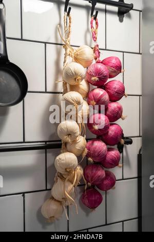 An der Wand der Wohnküche hängen Büschel roter und weißer Zwiebeln. Stockfoto