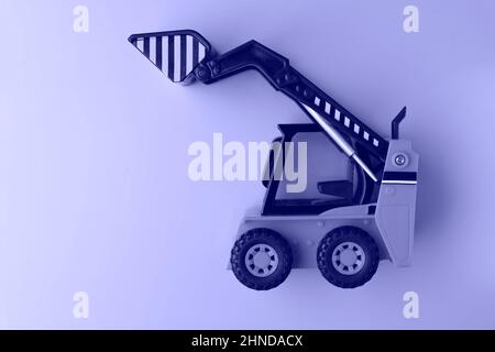 Spielzeug-Lader auf violettem Hintergrund, Mini-Lader, Spielzeug-Industrieauto, Kunststoff-Vorderrad-Lader., Foto in sehr peri Farbe getönt, Demonstration der t Stockfoto