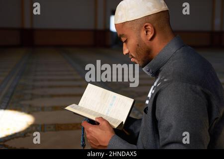Seitenansicht eines jungen muslimischen Mannes, der lächelte und den Koran las Stockfoto