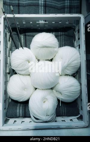 Kugeln mit weißen Wollfäden und Stricknadeln in einem Korb, Hausnadeln, Stricken, Wolle Stockfoto