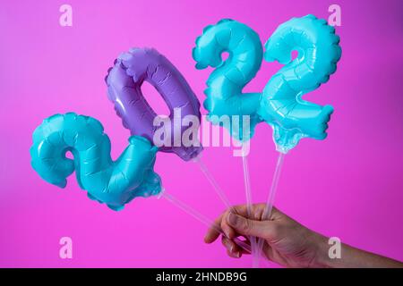 Eine Frauenhand hält aufblasbare Figuren mit den Zahlen 2022 auf purpurem Hintergrund, aufblasbare Ballons 2022, Neujahrskonzept und Weihnachtsdekor Stockfoto