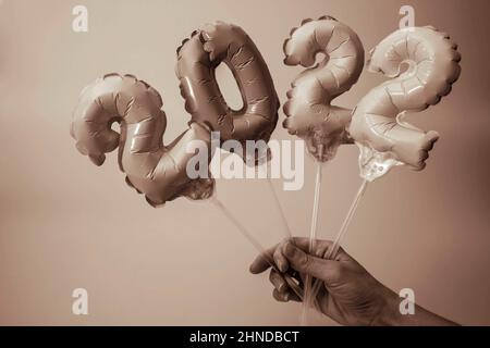 Eine Frauenhand hält aufblasbare Figuren mit Zahlen 2022, monochromes Bild, aufblasbare Kugeln 2022, Neujahrskonzept und Weihnachtsdekorationen, gree Stockfoto