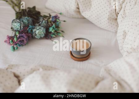Guten Morgen, Flat Lay Komposition mit Kaffeetasse, blauen Blumen und warmer Decke in gemütlichem Bett, Draufsicht. Stockfoto