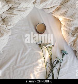 Guten Morgen, Flat Lay Komposition mit Kaffeetasse, blauen Blumen und warmer Decke in gemütlichem Bett, Draufsicht. Stockfoto