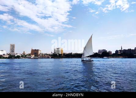 Ein Segelboot auf einem Flussspaziergang segelt entlang des Nils im Zentrum von Kairo zwischen den Wolkenkratzern und Attraktionen. Stockfoto