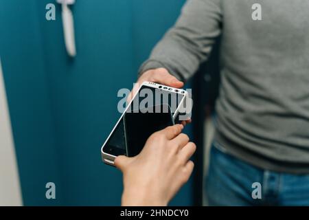 Nahaufnahme eines nicht erkennbaren Zustellers, der eine drahtlose POS-Konsole zur kontaktlosen Zahlung per Handykarte an eine junge Frau gab Stockfoto
